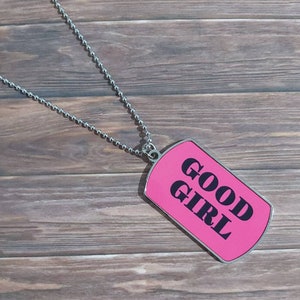 May include: A silver chain necklace with a pink dog tag pendant that says "GOOD GIRL" in black letters.