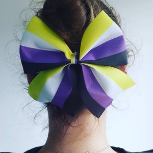 Op de afbeelding: Een grote gele, witte, paarse en zwarte strik met een gestreept patroon. De strik is in een knoop geknoopt en wordt in het haar gedragen.