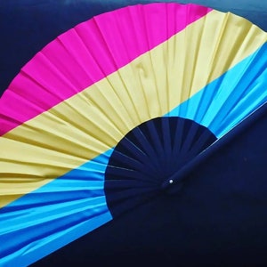 May include: A hand fan with a black handle and a colorful fabric design. The fabric is pink, yellow, and blue.