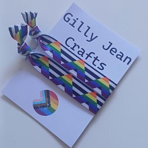 May include: Two hair ties with a rainbow geometric pattern and black and white stripes. The hair ties are next to a white card with the text "Gilly Jean Crafts" and a rainbow logo.