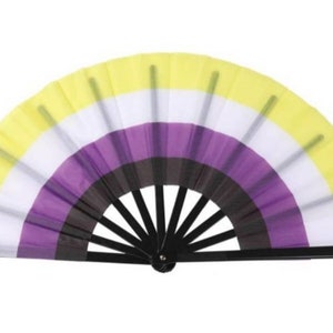 Pode incluir: Um leque de mão amarelo, branco, roxo e preto com uma alça preta. O leque é decorado com as cores da bandeira do orgulho não binário.