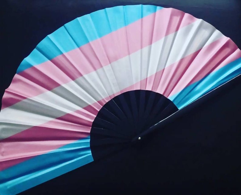 May include: A hand fan with a blue, pink, and white striped design. The fan is made of fabric and has a black wooden handle.
