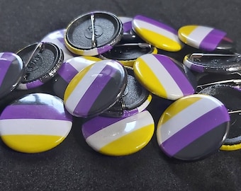 May include: A close-up of a pile of round, pin-back buttons with a yellow, white, and purple striped design. The buttons are arranged in a random pattern.