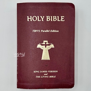 Puede incluir: Una Santa Biblia de color burdeos con letras doradas y un emblema dorado. La portada dice "HOLY BIBLE" encima de "TBN's Parallel Edition". Debajo del emblema, dice "KING JAMES VERSION and THE LIVING BIBLE".