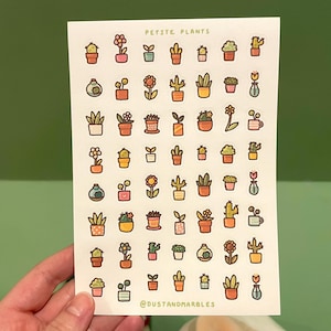 May include: A sheet of stickers featuring various petite plants in pots. The stickers include cacti, flowering plants, and other small potted greenery. The text "PETITE PLANTS" is at the top. The artist's name, "@dustandmarbles", is at the bottom.