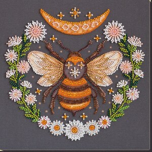 May include: A beaded embroidery design of a bee with wings outstretched, surrounded by a crescent moon and floral motifs. The bee is brown and yellow with a white and black pattern on its back. The flowers are pink, white, and green.