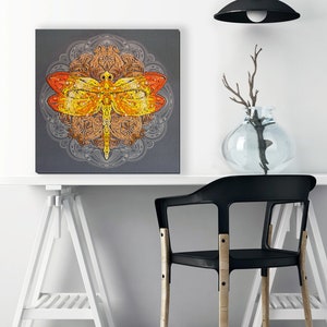 May include: A square canvas print featuring a colorful dragonfly with intricate details against a gray background. The dragonfly is surrounded by a mandala design.