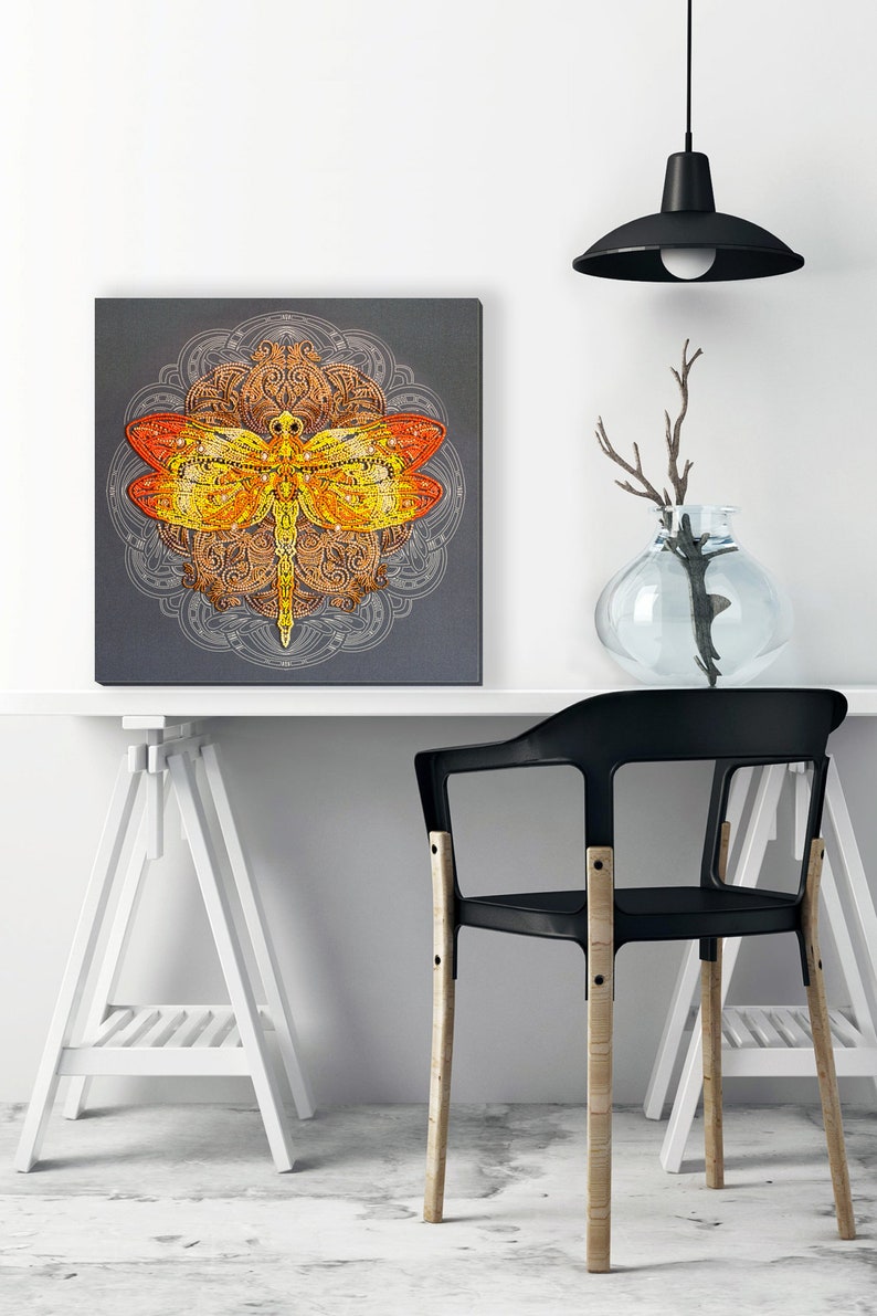 May include: A square canvas print featuring a colorful dragonfly with intricate details against a gray background. The dragonfly is surrounded by a mandala design.