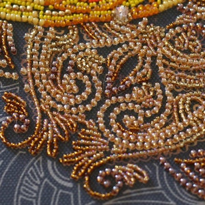 May include: Close-up of a beaded design with a swirling pattern. The beads are a mix of gold, brown, and beige colors.