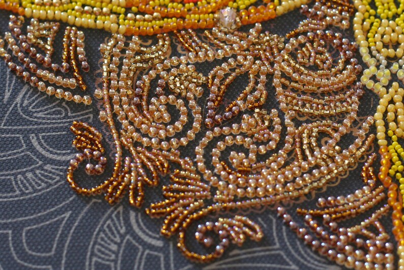 May include: Close-up of a beaded design with a swirling pattern. The beads are a mix of gold, brown, and beige colors.