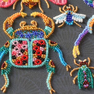 May include: A colorful beaded beetle with turquoise, red, pink, gold, and black beads. The beetle is a decorative piece and is made with a variety of beads.