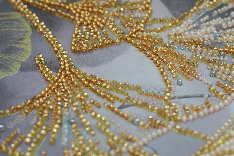 May include: Close-up of a fabric with gold and white beads sewn in a pattern. The beads are arranged in a floral design.