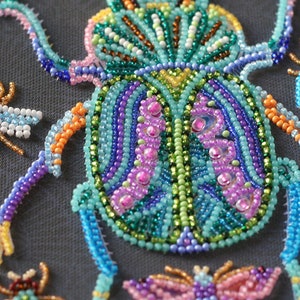 May include: A close-up of a beaded beetle with a blue, green, and purple body. The beetle is surrounded by smaller beaded insects, including bees and butterflies.