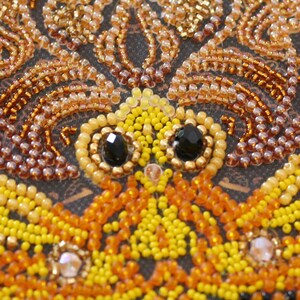 May include: Close-up of a beaded artwork featuring a butterfly with yellow, orange, and brown beads. The butterfly has black bead eyes.