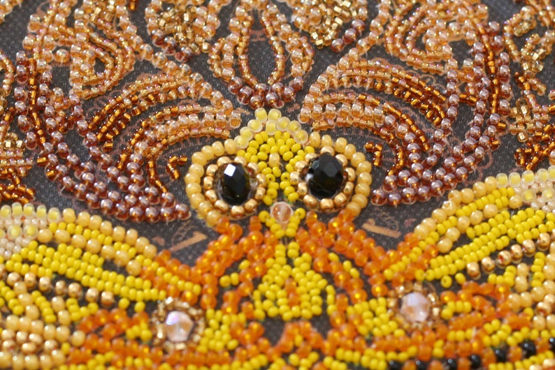 May include: Close-up of a beaded artwork featuring a butterfly with yellow, orange, and brown beads. The butterfly has black bead eyes.