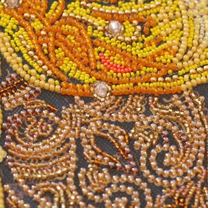 May include: Close-up of a beaded artwork with a swirling pattern of yellow, orange, and red beads. The beads are arranged in a tight, intricate design, creating a textured surface.