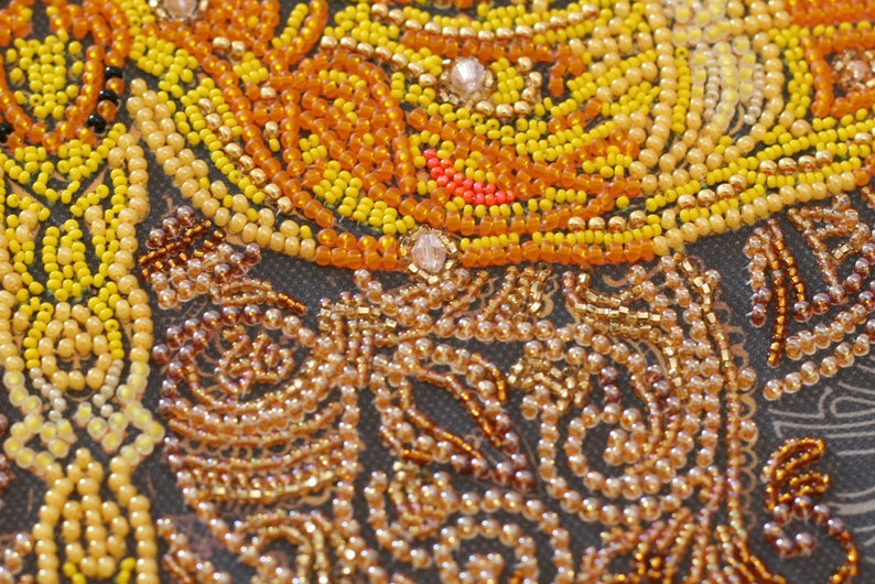 May include: Close-up of a beaded artwork with a swirling pattern of yellow, orange, and red beads. The beads are arranged in a tight, intricate design, creating a textured surface.