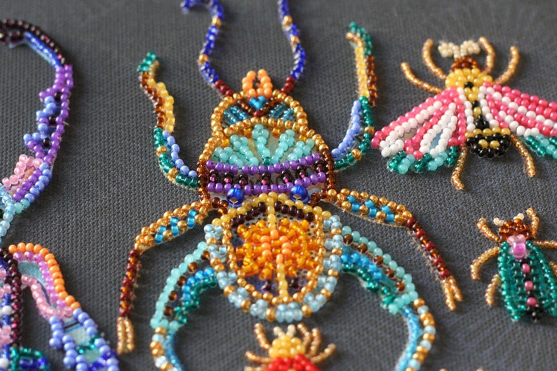 May include: Close-up of a beaded insect with a colorful design. The insect is made of small, colorful beads and has a detailed pattern. The insect is surrounded by other beaded insects, including a bee and a ladybug.