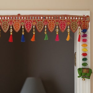 May include: A colorful door hanging with red fabric, gold trim, and mirrored accents. It features a row of tassels in various colors, including blue, green, orange, and yellow. The hanging is decorated with small, beaded leaves.