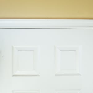 May include: A white door with a brass door handle. Two colorful strings of fabric elephants hang on either side of the door.