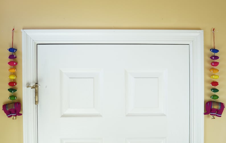 May include: A white door with a brass door handle. Two colorful strings of fabric elephants hang on either side of the door.