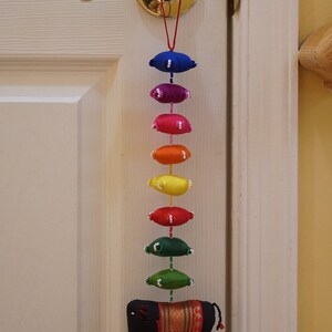 May include: A rainbow-colored fabric garland with a black elephant charm hanging from a door knob. The garland is made of small, round fabric pieces sewn together with white beads.