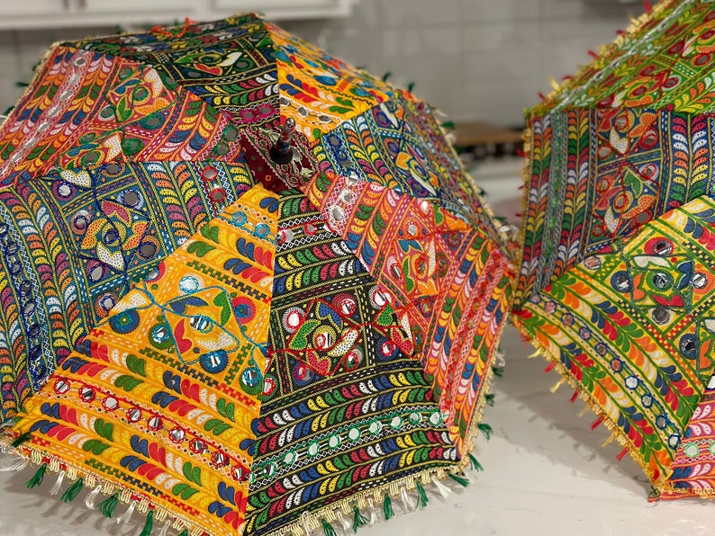 May include: Two colorful, patchwork-style umbrellas with intricate patterns and mirrored accents. The umbrellas feature a variety of vibrant colors, including yellow, red, blue, and green, with decorative tassels along the edges. These decorative umbrellas are perfect for adding a pop of color.