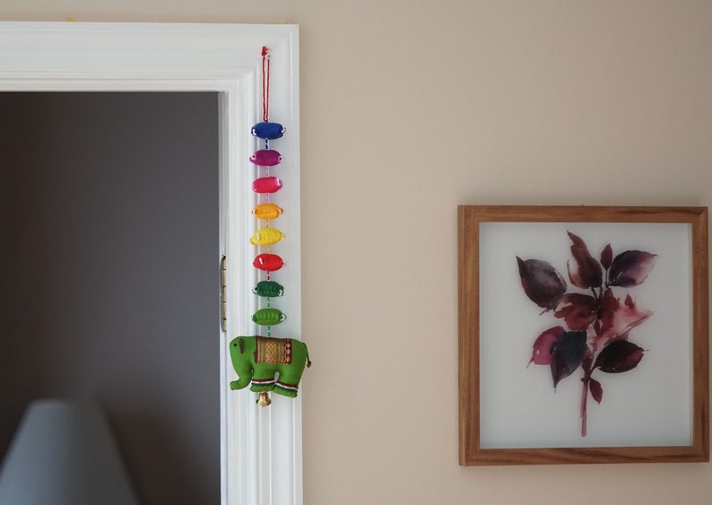 May include: A colorful door hanging with a rainbow of fabric ovals and a green felt elephant at the bottom.