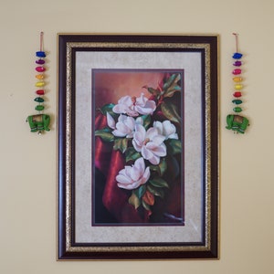 May include: Framed painting of white magnolia flowers with green leaves on a red background.