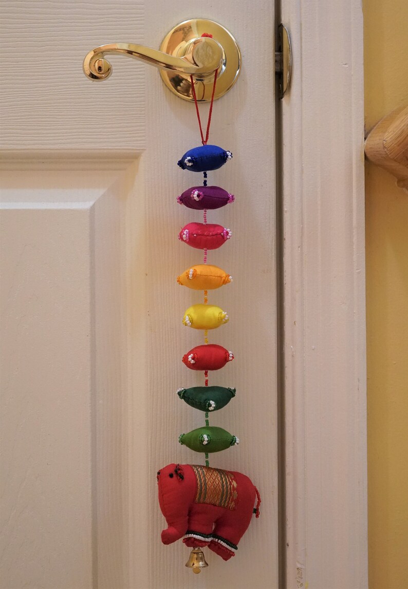 May include: A colorful door hanging with a red elephant at the bottom. The hanging features a series of fabric ovals in rainbow colors, each with white beads around the edges.