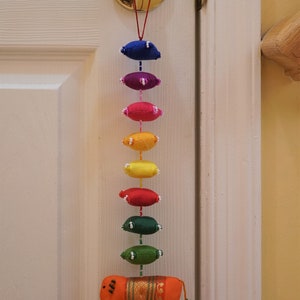 May include: A colorful door hanging with a rainbow of fabric ovals and a small orange elephant with a bell at the bottom.