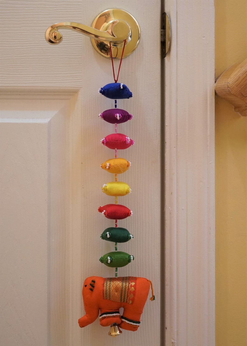 May include: A colorful door hanging with a rainbow of fabric ovals and a small orange elephant with a bell at the bottom.
