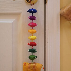 May include: A yellow felt elephant with gold trim hangs from a door knob. A string of colorful felt ovals in rainbow colors hangs from the elephant.
