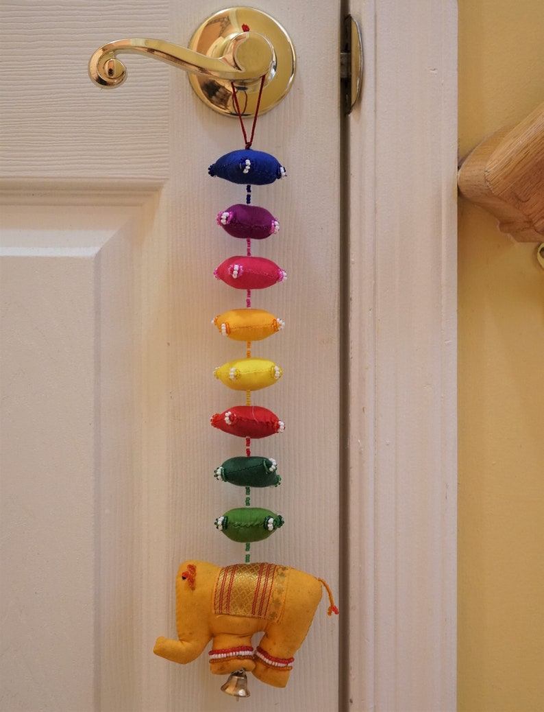 May include: A yellow felt elephant with gold trim hangs from a door knob. A string of colorful felt ovals in rainbow colors hangs from the elephant.