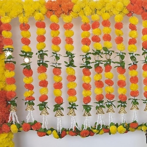 May include: A garland of yellow and orange marigold flower pom-poms with small bells hanging from the bottom.