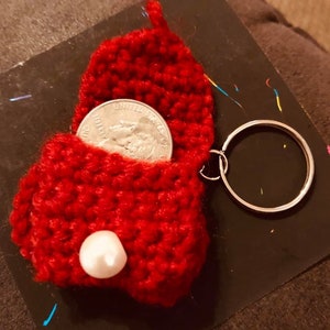 May include: Red crocheted heart-shaped keychain with a silver coin inside and a white pearl bead. The keychain has a silver ring.