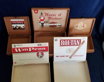 May include: Five vintage cigar boxes with various brand names and prices. The boxes are made of wood and have a light brown color. The boxes are open and show the inside of the boxes. The boxes are arranged in a row. The boxes are all different sizes. The boxes are all in good condition.