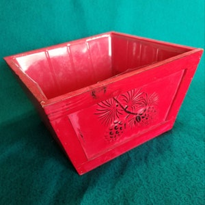May include: A red wooden planter with a pine cone design. The planter is square and has a slightly flared lip.