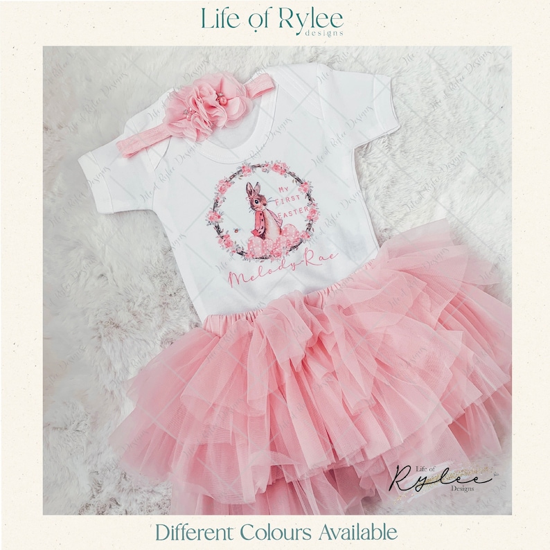 May include: A pink tulle tutu skirt and a white onesie with a bunny rabbit graphic and the text "My First Easter" and "Melody-Rae".