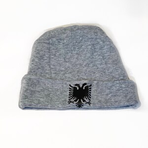 May include: A gray beanie with a black double-headed eagle emblem on the front.