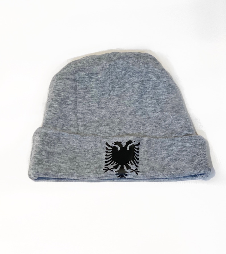 May include: A gray beanie with a black double-headed eagle emblem on the front.