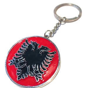 Könnte beinhalten: Ein roter und schwarzer Schlüsselanhänger aus Metall mit dem albanischen Doppelkopfadler.