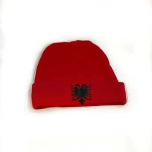 May include: A red beanie with a black Albanian eagle emblem.