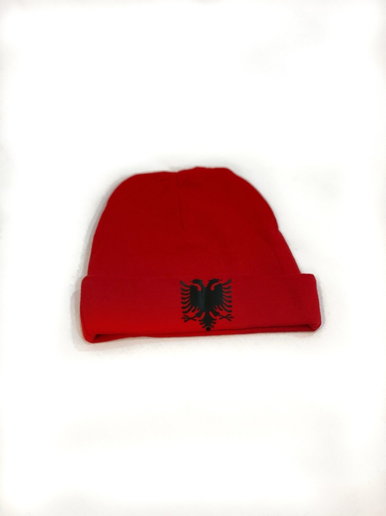 May include: A red beanie with a black Albanian eagle emblem.