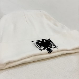 May include: White beanie with a black embroidered Albanian eagle.