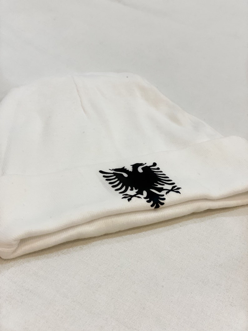 May include: White beanie with a black embroidered Albanian eagle.