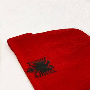 May include: Red beanie with a black Albanian eagle emblem.