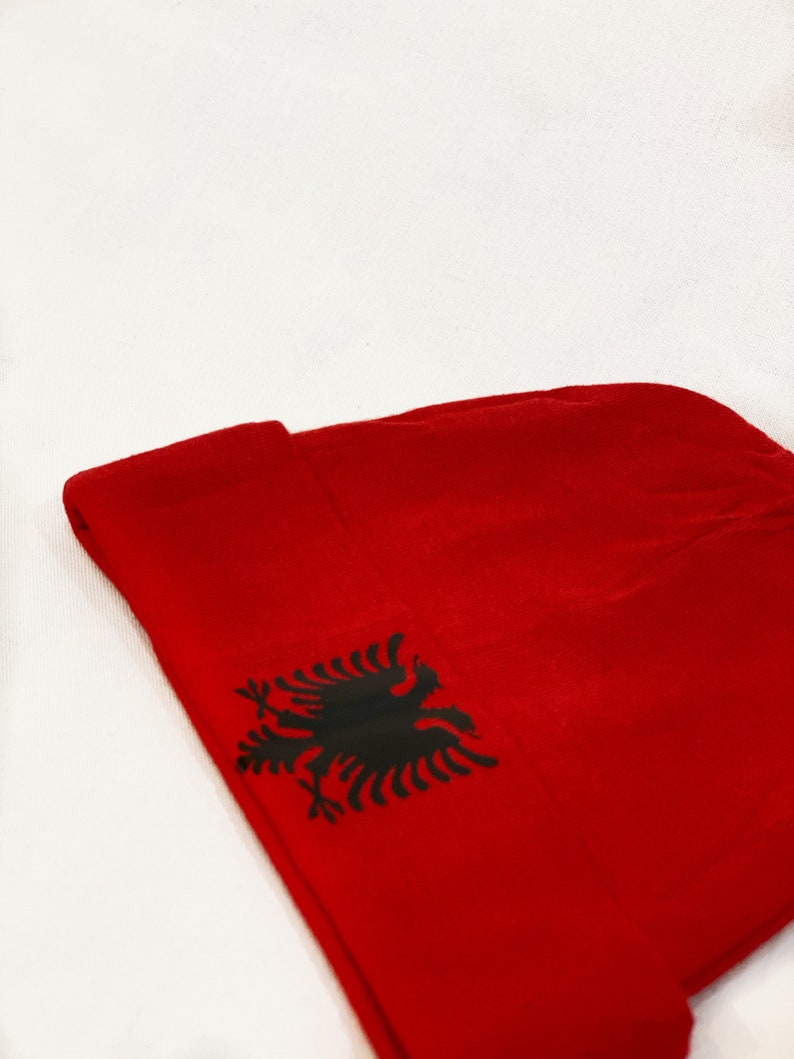 May include: Red beanie with a black Albanian eagle emblem.