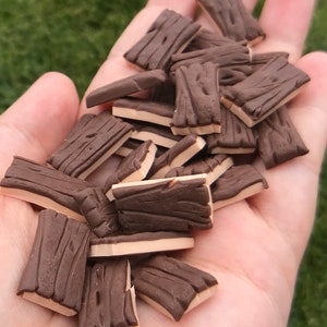 May include: A pile of small, brown and beige wooden plank-shaped polymer clay charms. The charms are about 1 inch long and 1/2 inch wide.