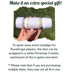 May include: A white Christmas cracker with gold accents. The cracker is being held in a hand. The text "Make it an extra special gift!" is at the top of the image. The text "To spark some extra nostalgia for RuneScape players, this item can be wrapped in a white Christmas Cracker, reminiscent of the in-game rare item!** Please note that if you are purchasing multiple items, they may not all fit in one cracker (but I'm willing to try upon request)" is at the bottom of the image.